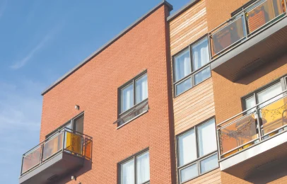 Moderne bygning med røde mursten og balkoner, der illustrerer vigtigheden af løbende vedligeholdelse af ejendomme.