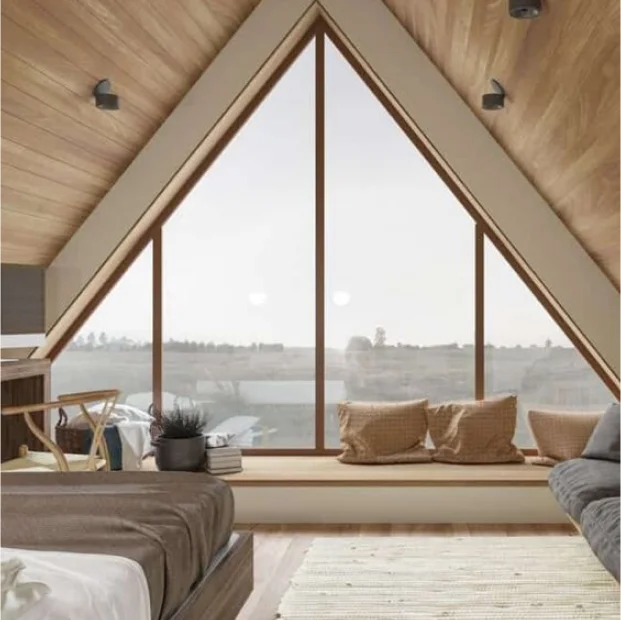 Hyggeligt loftshjørne med store trekantede vinduer og træfinish, fremviser detaljeret tømrerarbejde i hjemmet med udsigt over landskabet.